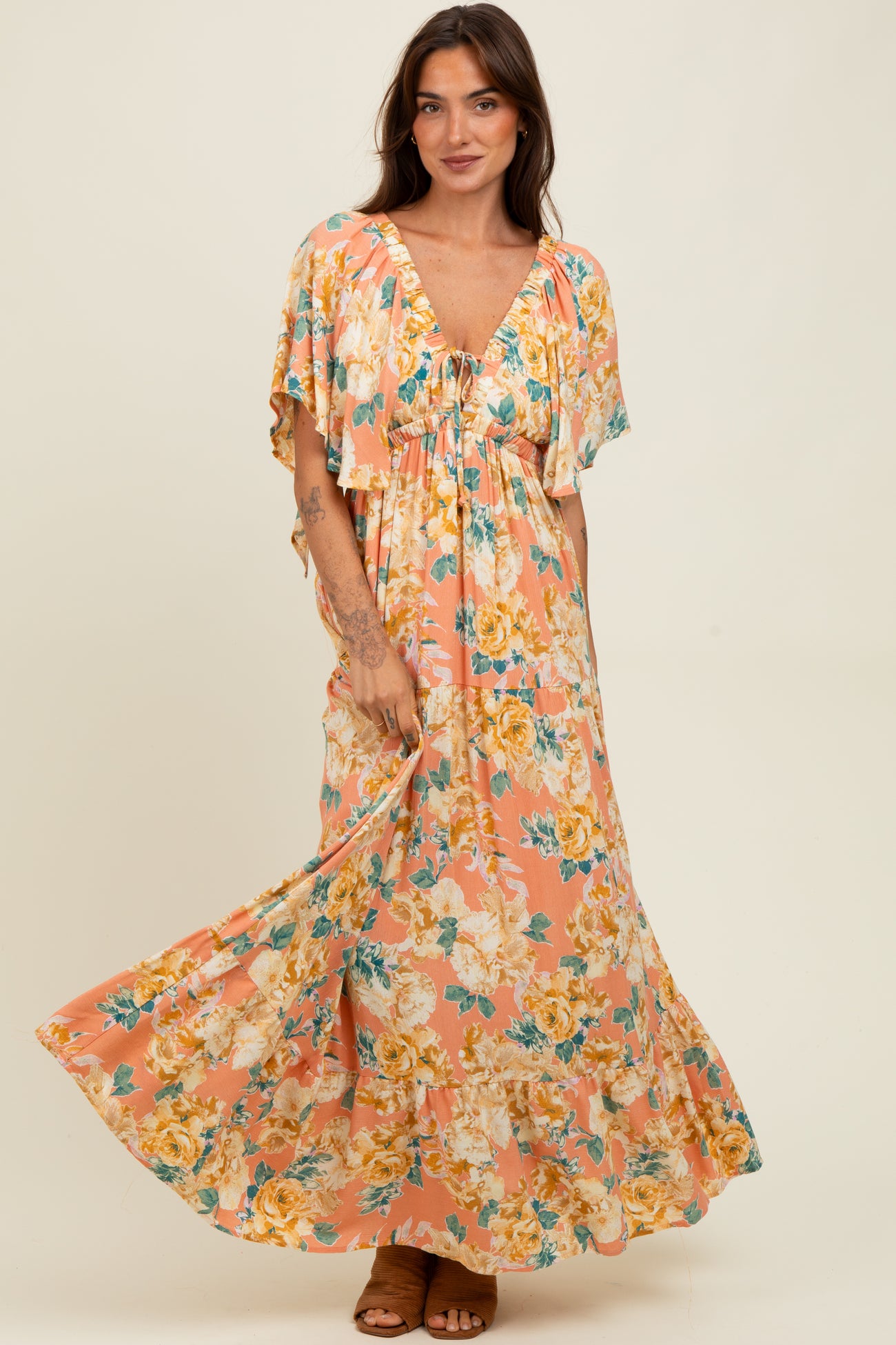woman wearing a floral maxi dress with cap sleeves and a deep neckline, standing and smiling