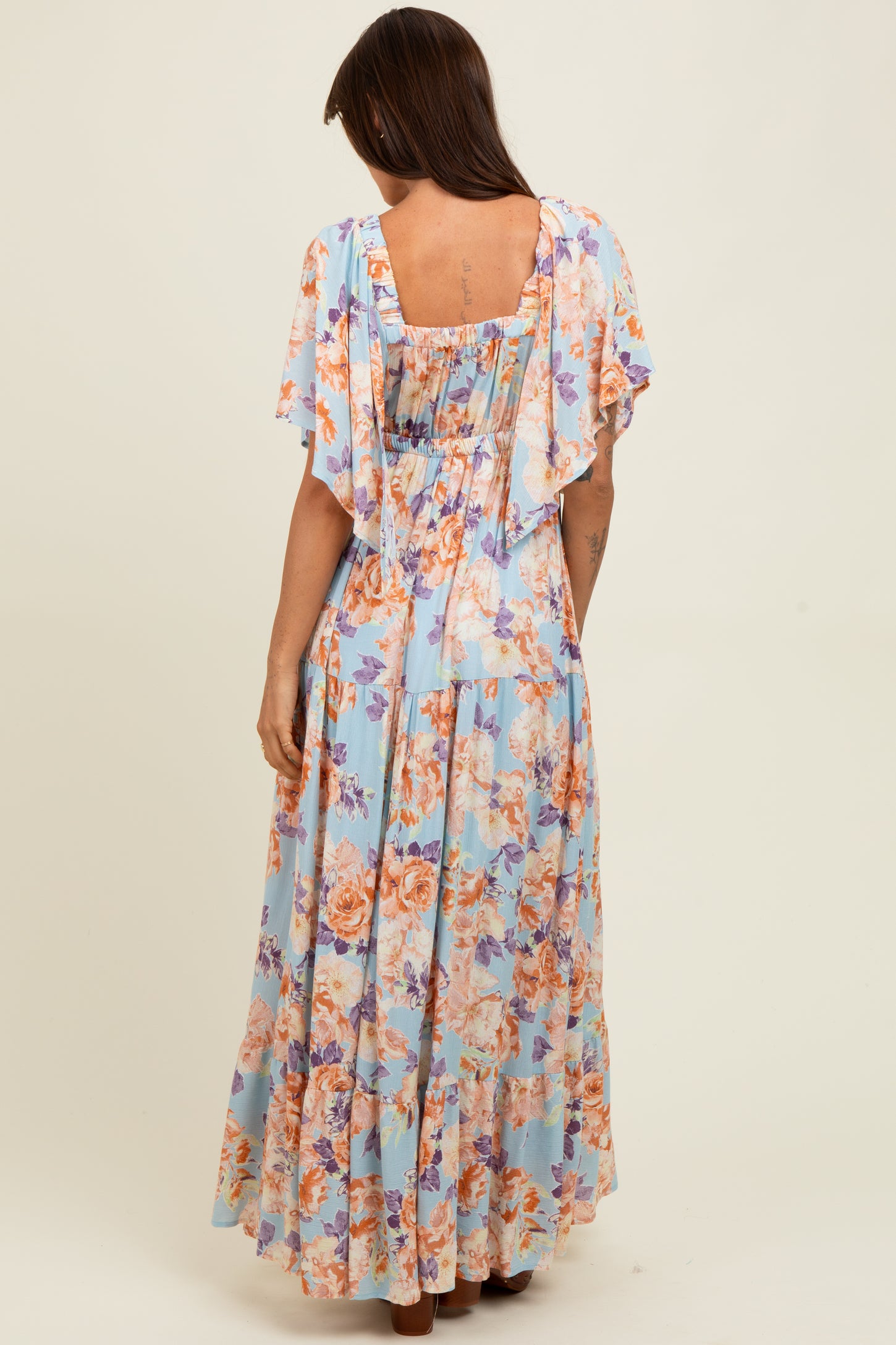 woman wearing a floral maxi dress in light blue with flutter sleeves and a ruched back design
