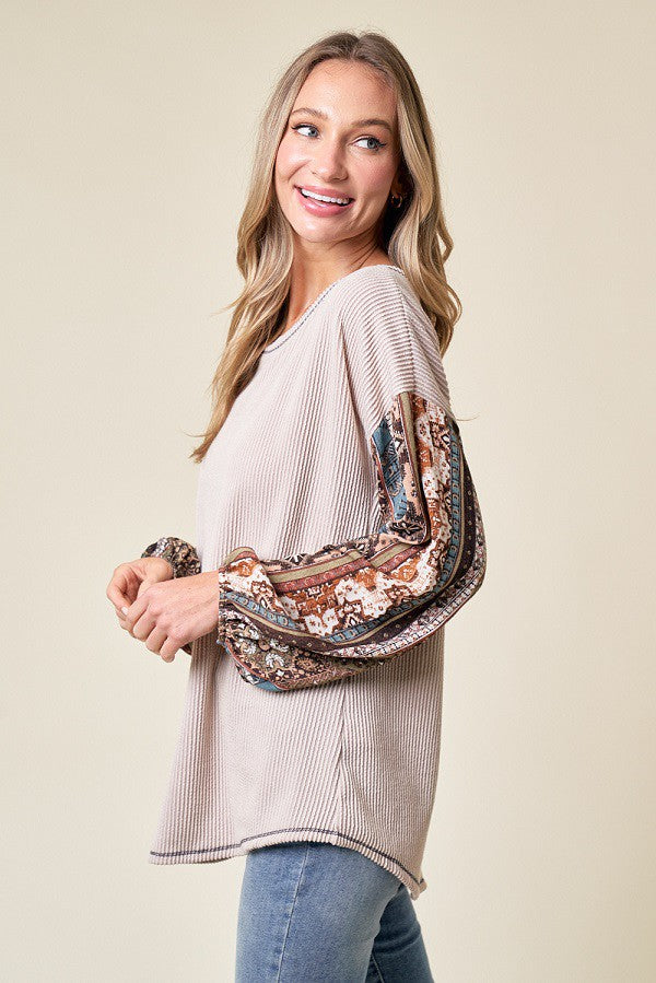woman wearing a beige ribbed top with patterned bell sleeves and smiling against a neutral background