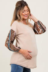 woman wearing a beige ribbed maternity top with patterned long sleeves and holding her baby bump