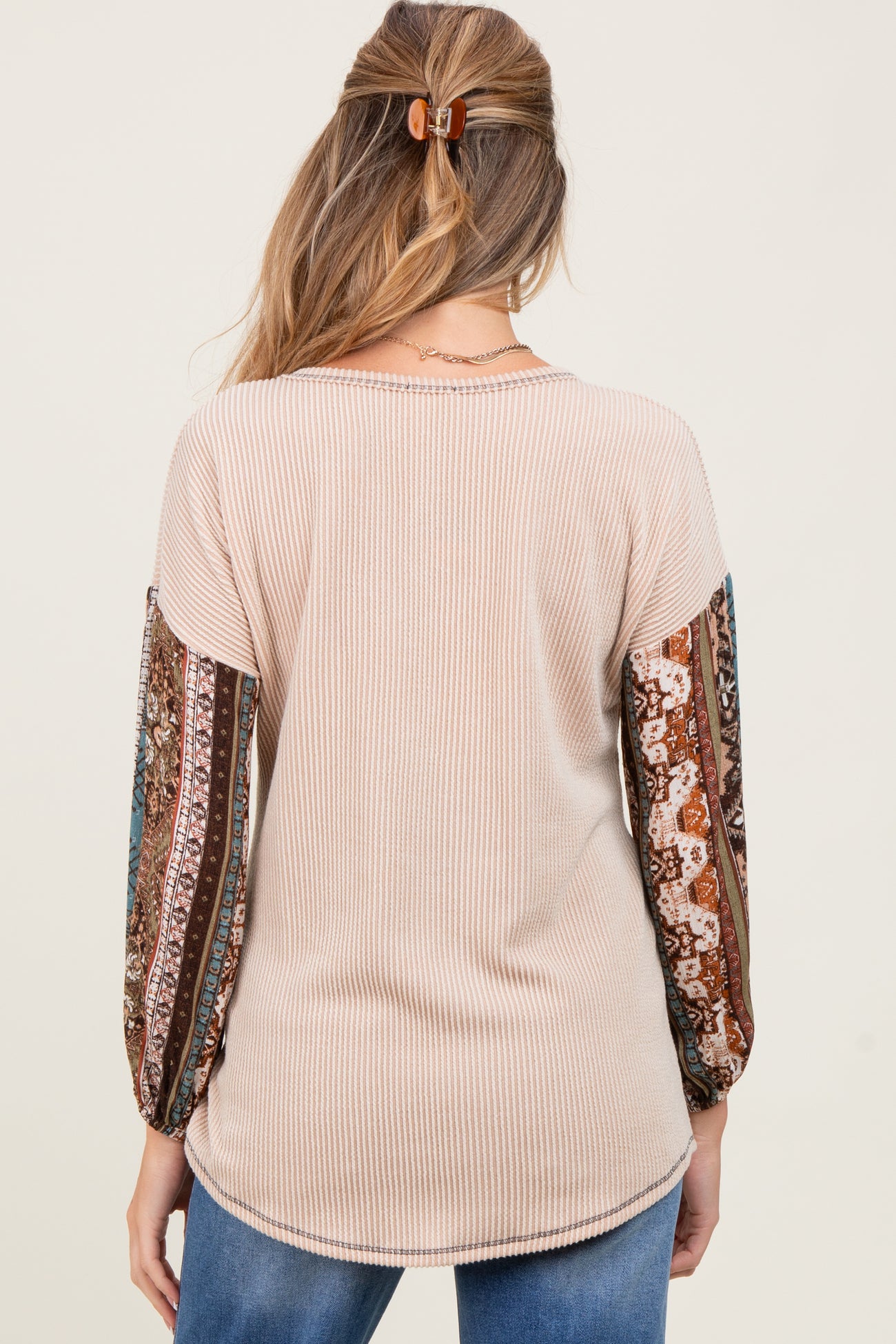 woman wearing a cream ribbed maternity top with patterned balloon sleeves and a curved hem