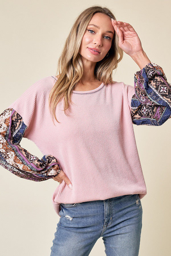 woman wearing a pink ribbed long sleeve top with patterned bell sleeves and blue jeans