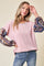 woman wearing a pink ribbed long sleeve top with patterned bell sleeves and blue jeans