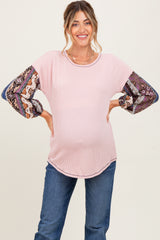 woman wearing a pink maternity top with patterned long sleeves and a visible baby bump, posing with hands on hips