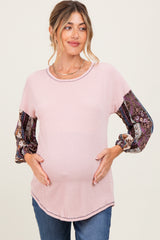 woman wearing a light pink maternity top with patterned long sleeves and holding her baby bump