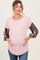 woman wearing a light pink maternity top with patterned long sleeves and holding her baby bump