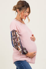 woman wearing a light pink long sleeve maternity top with patterned sleeves and holding her baby bump
