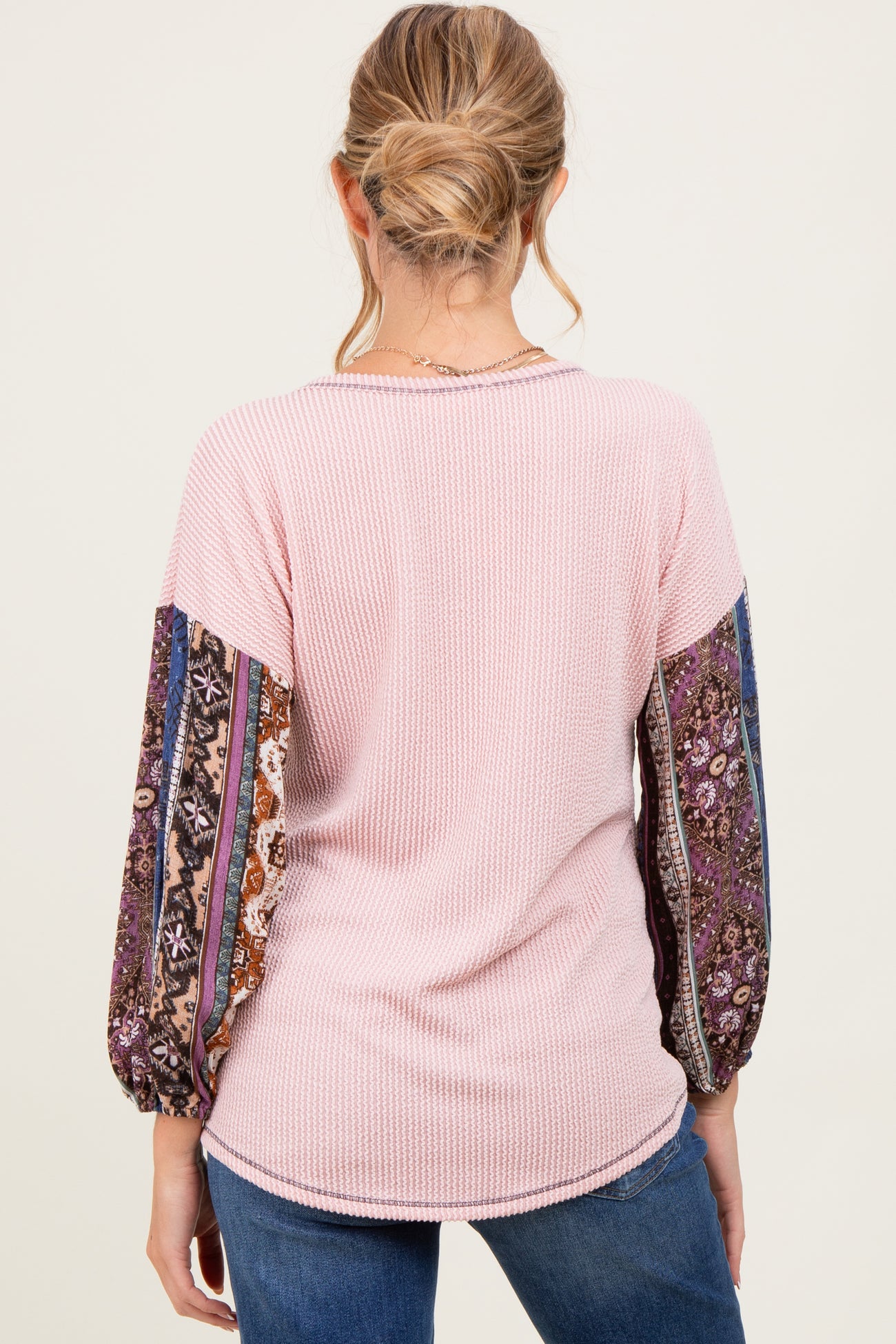 woman wearing a pink ribbed maternity top with patterned balloon sleeves, seen from the back