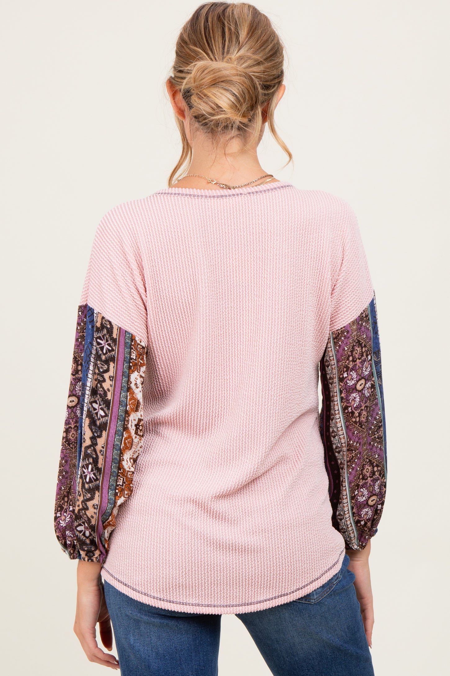 woman wearing a pink ribbed maternity top with patterned balloon sleeves, seen from the back