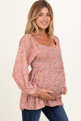 woman wearing a rust colored floral print maternity top with smocked details and holding her baby bump