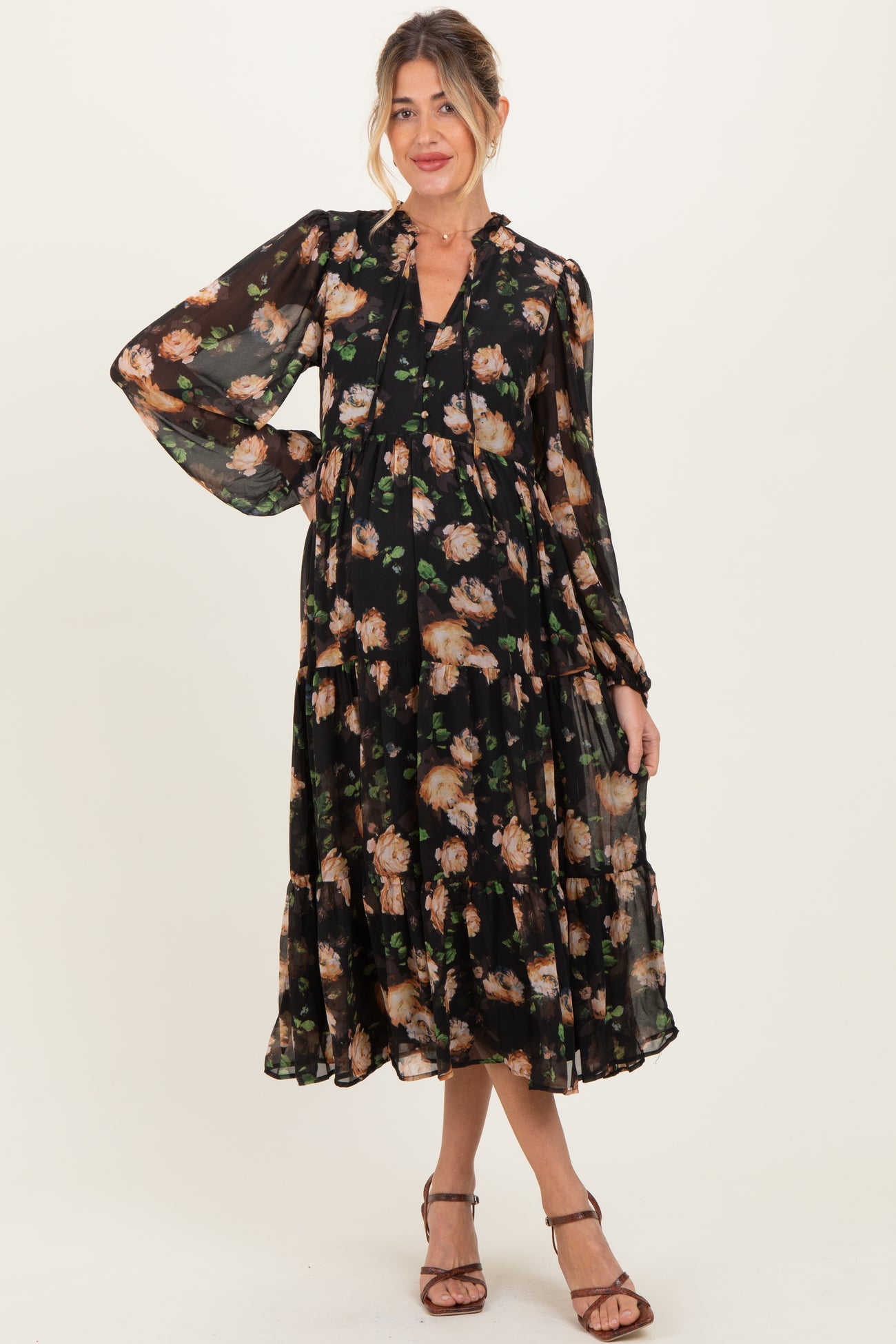 woman wearing a black floral maternity maxi dress with long sleeves and tiered ruffles, posing with a smile
