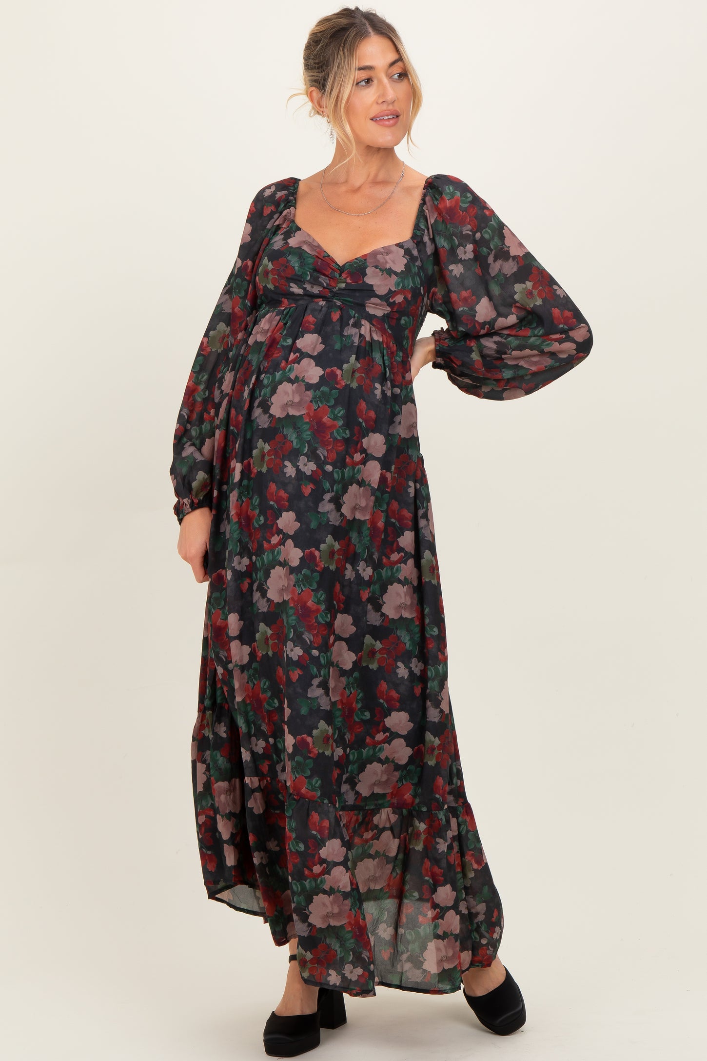 woman wearing a dark floral maternity maxi dress with long sleeves and a visible baby bump
