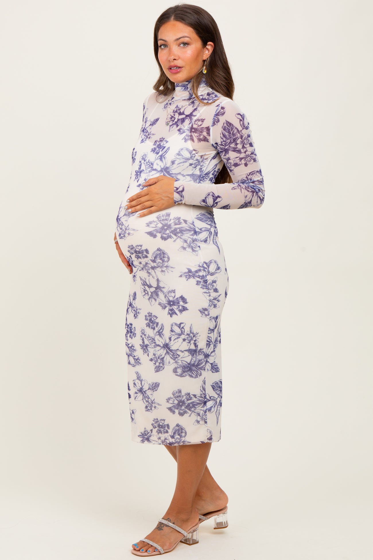 woman wearing a sheer long sleeve maternity dress with purple floral print and holding her baby bump