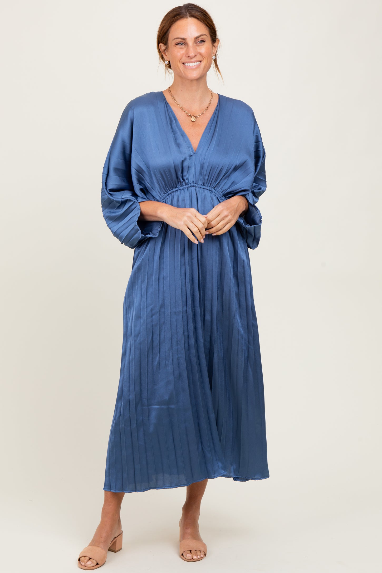 woman wearing a pleated blue maxi dress with a deep v-neck and long sleeves