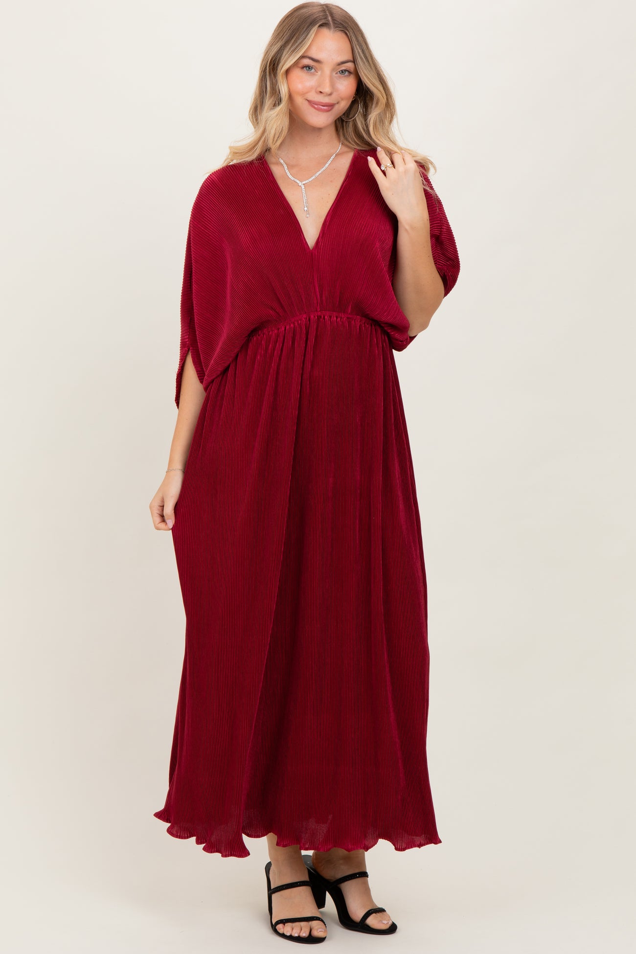 woman wearing a deep red maxi dress with a v-neckline and flowy sleeves, styled with black block heels