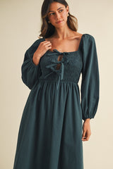 woman wearing a dark green smocked dress with a square neckline and long puff sleeves