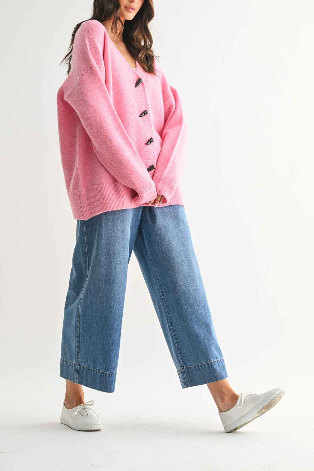 woman wearing a pink oversized cardigan with buttons and wide-leg blue jeans, styled with white sneakers