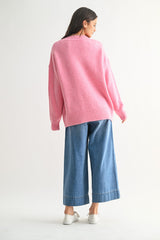 woman wearing a loose-fitting pink sweater and wide-leg blue denim jeans, standing with her back to the camera