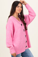 woman wearing a bright pink oversized cardigan with a v-neck and black buttons, styled with blue jeans