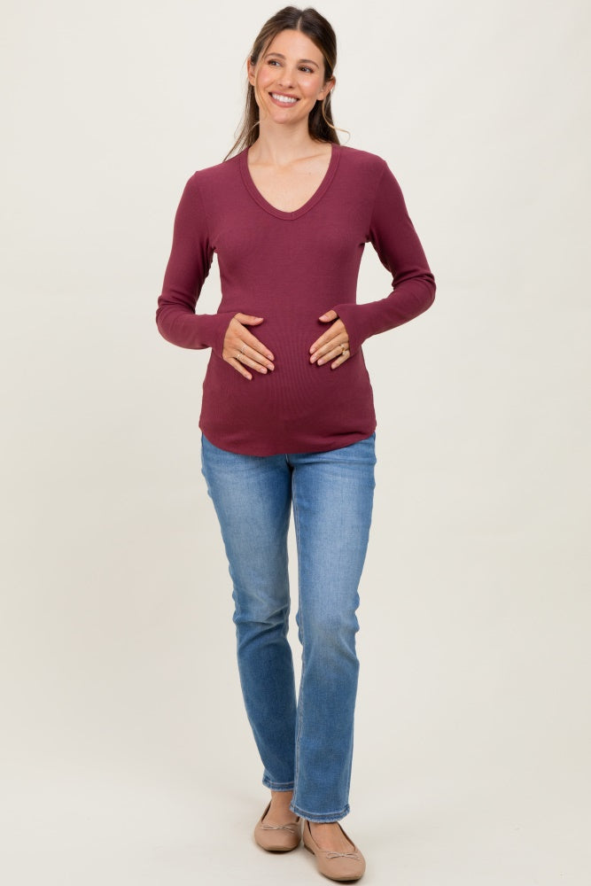 woman wearing a burgundy long sleeve maternity top and holding her baby bump, paired with blue jeans