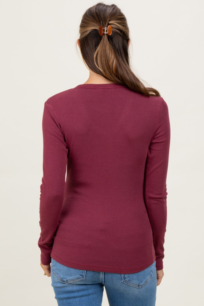 woman wearing a burgundy long sleeve maternity top, viewed from the back, with her hair tied up and blue jeans