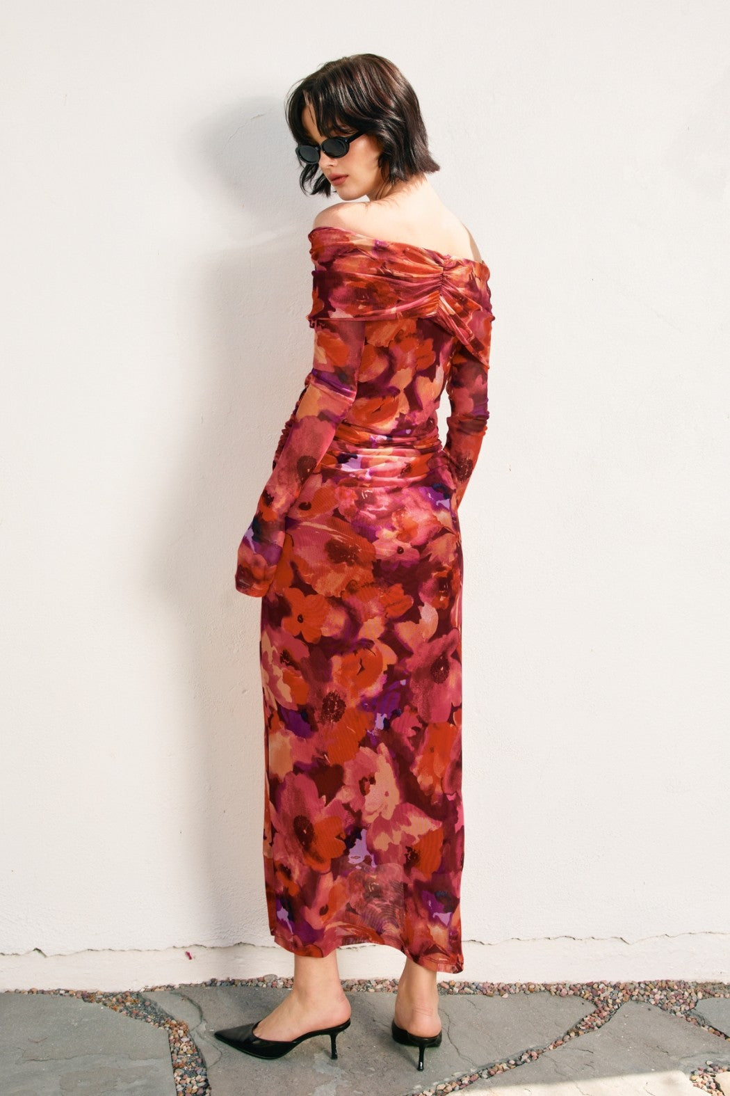woman wearing a vibrant floral off-the-shoulder dress with long sleeves and a fitted silhouette, styled with sunglasses