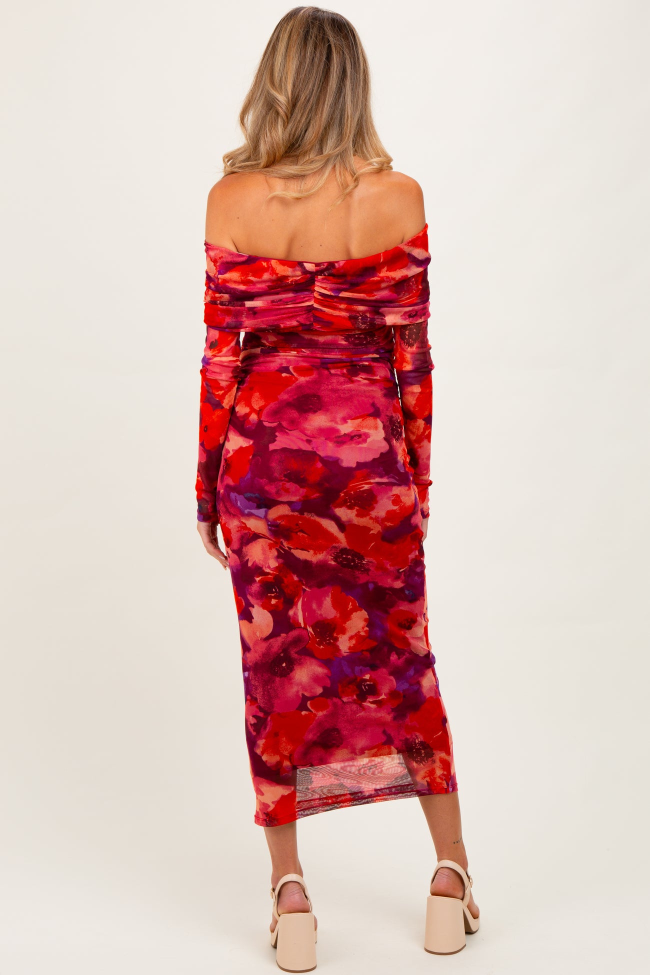 woman wearing a red floral off-shoulder maternity dress with long sleeves, showing a silhouette of a baby bump