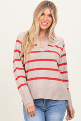 woman wearing a beige striped sweater with red stripes and a v-neckline, paired with blue jeans