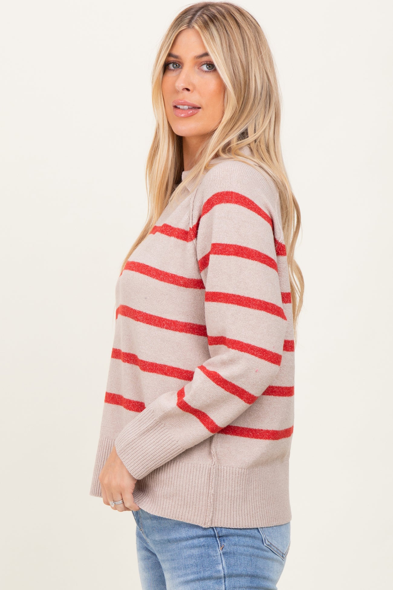 woman wearing a beige sweater with red stripes and a relaxed fit, standing sideways with long blonde hair