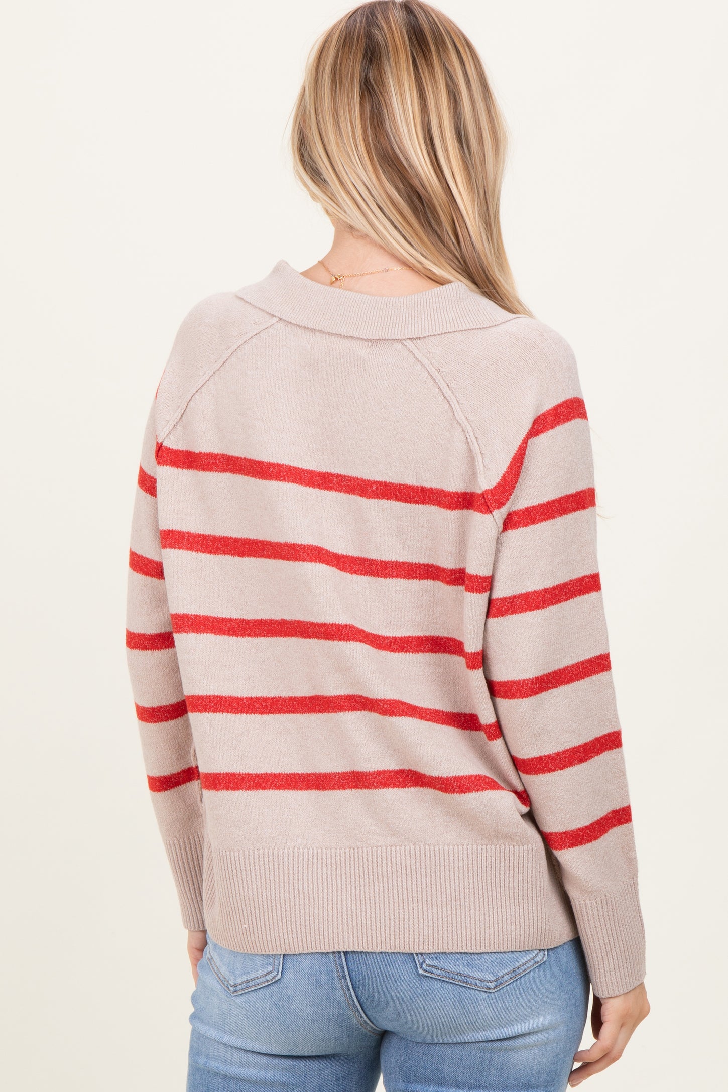woman wearing a beige sweater with red stripes, shown from the back, paired with blue jeans