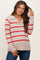 woman wearing a beige maternity sweater with red stripes and a v-neckline, smiling and touching her hair