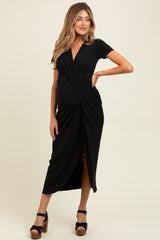 woman wearing a black short sleeve maternity dress with a twist front and side slit, showcasing her baby bump