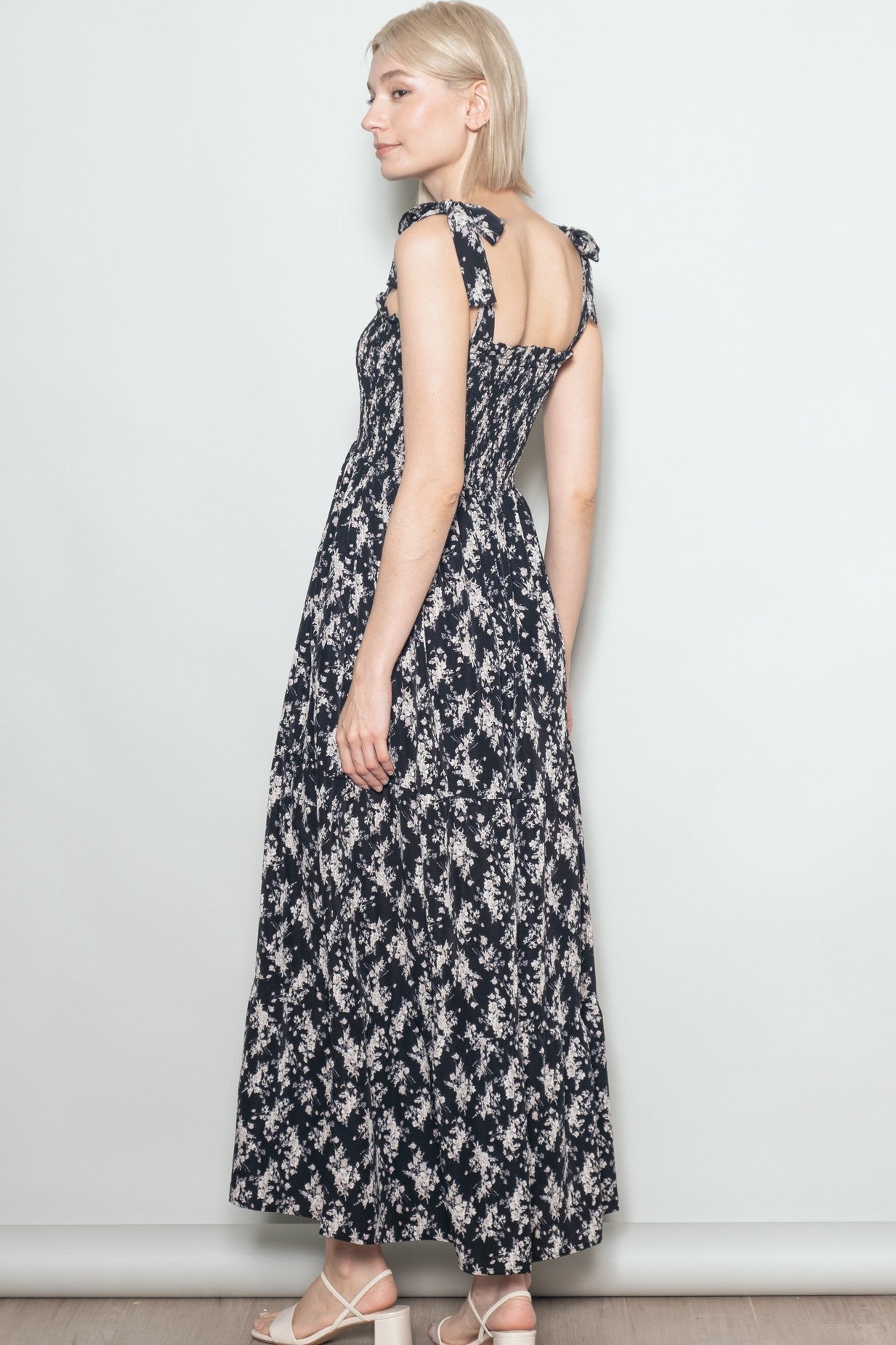 woman wearing a navy blue floral maxi dress with shoulder ties, showing the back view