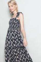 woman wearing a black floral maxi dress with smocked bodice and tie straps, standing in a neutral backdrop