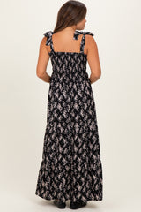 woman wearing a black maternity maxi dress with floral print and tie straps, showing a baby bump from the back