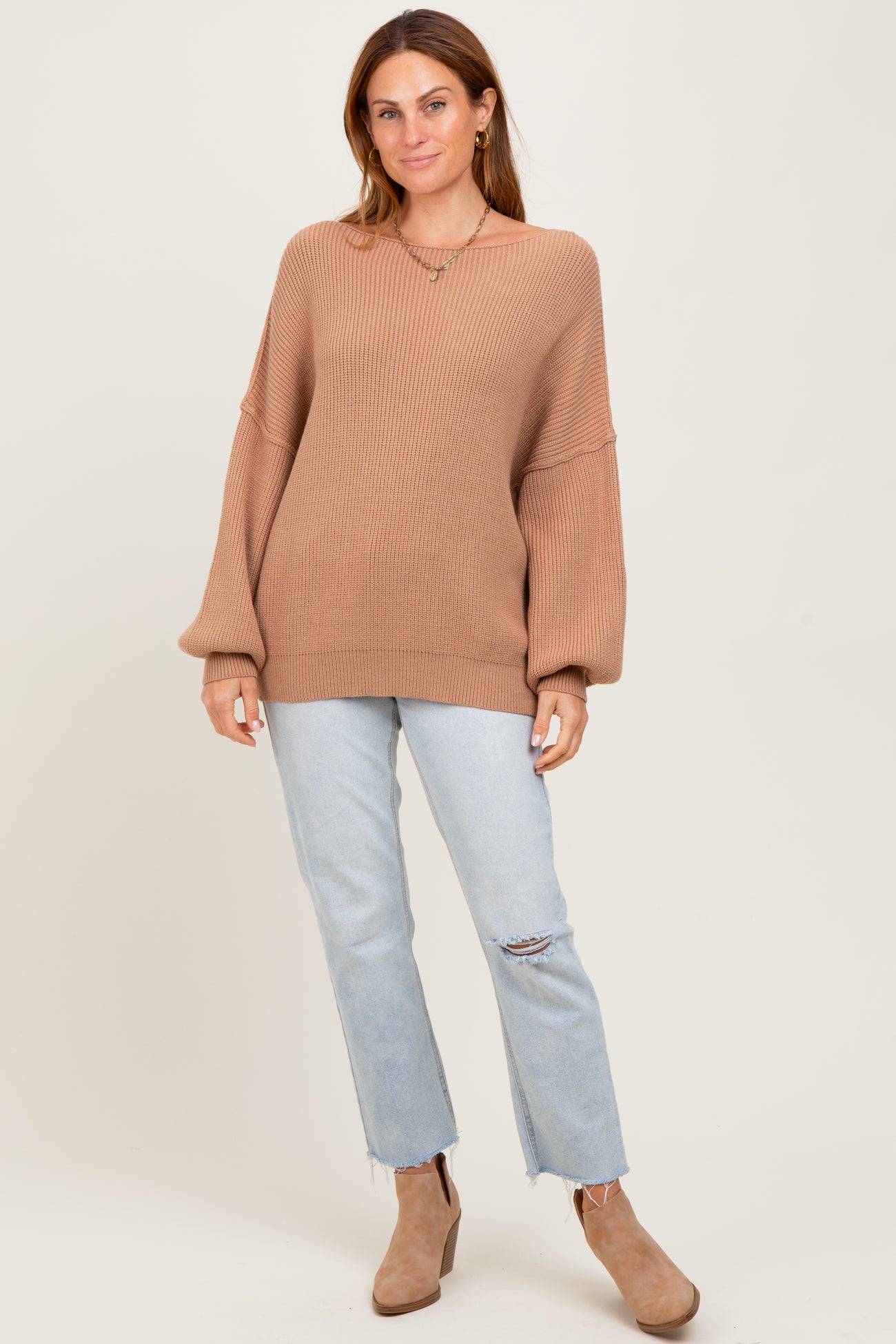 woman wearing a light brown oversized ribbed sweater and light blue distressed jeans with heeled ankle boots