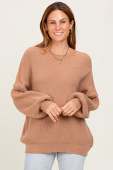 woman wearing a light brown oversized ribbed sweater with wide sleeves, smiling against a neutral background