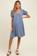 woman wearing a blue maternity dress with puff sleeves and button details, showing a baby bump