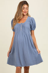 woman wearing a dusty blue maternity dress with puff sleeves and button detailing, showcasing her baby bump