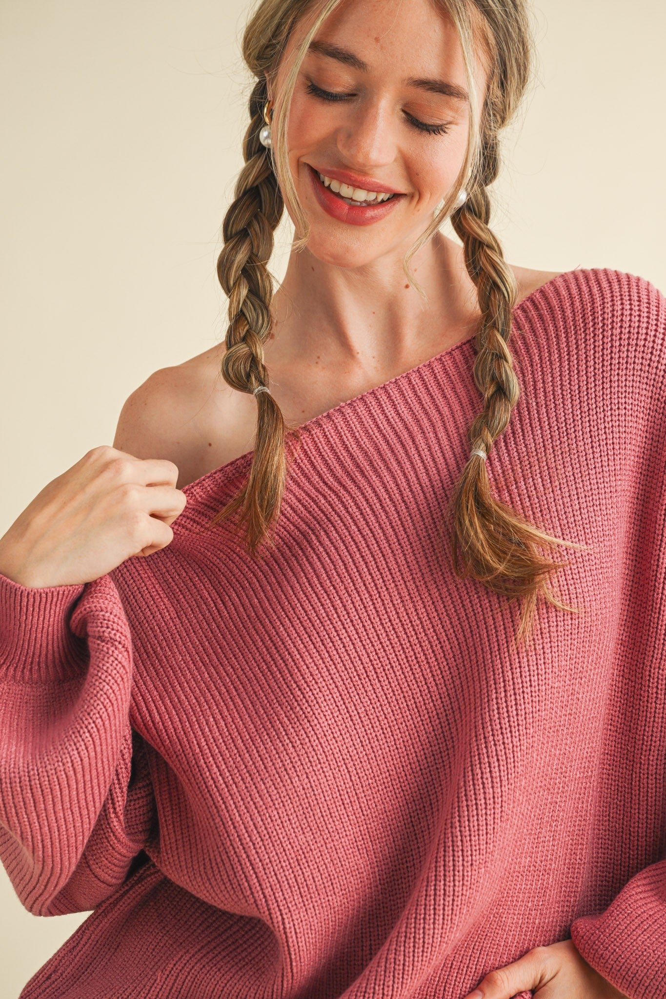 woman wearing an oversized coral pink off-the-shoulder sweater with a ribbed texture and braided hair