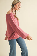 woman wearing a pink oversized sweater with bell sleeves and blue high-waisted jeans, in motion