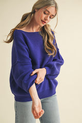 woman wearing a purple oversized sweater with relaxed sleeves and a wide neckline, paired with light blue jeans