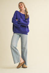 woman wearing a purple oversized knit sweater and light wash wide-leg jeans, standing with arms crossed