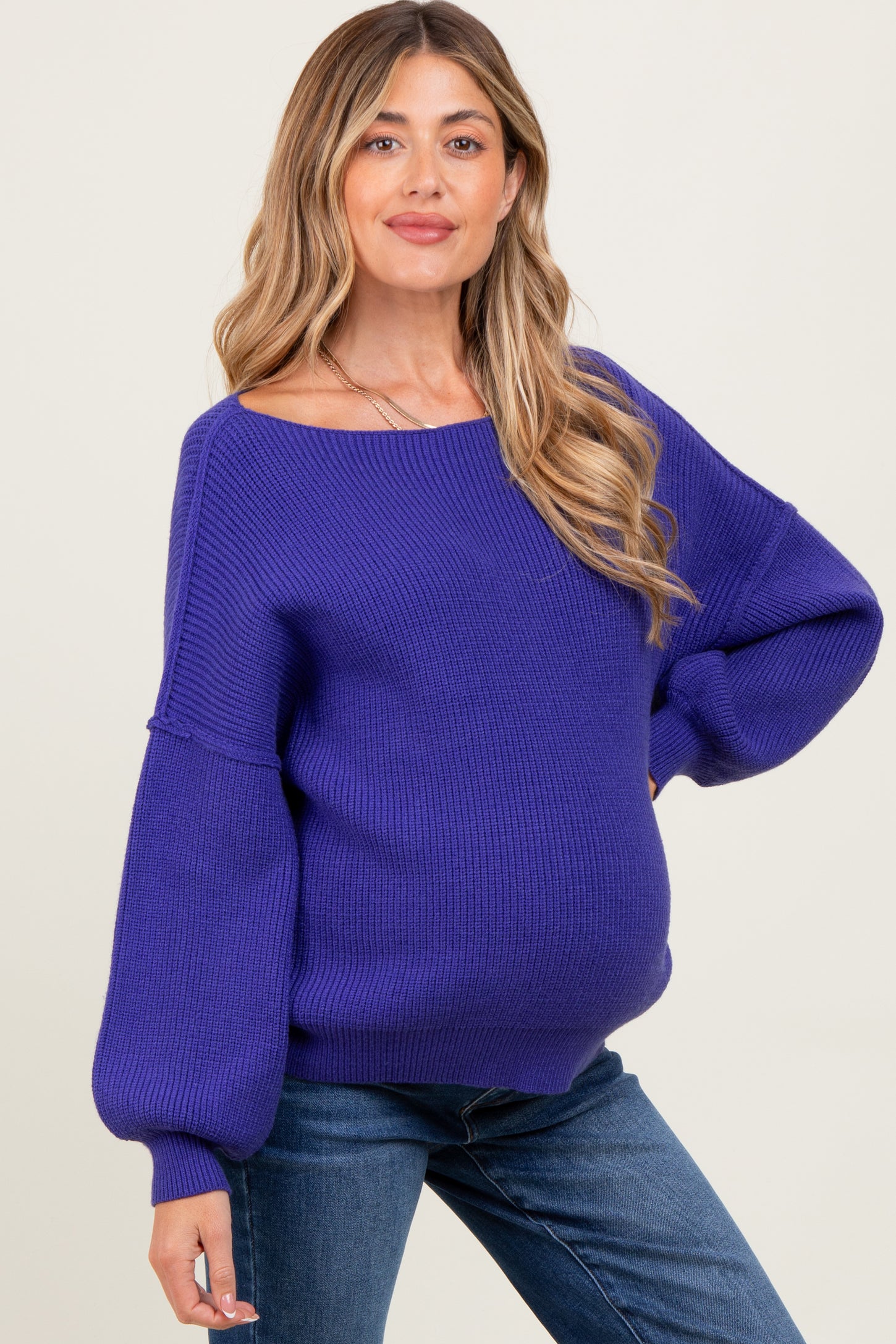 woman wearing a purple oversized maternity sweater and showing her baby bump, paired with denim jeans