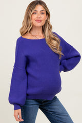 woman wearing a purple oversized maternity sweater and showing her baby bump, paired with denim jeans