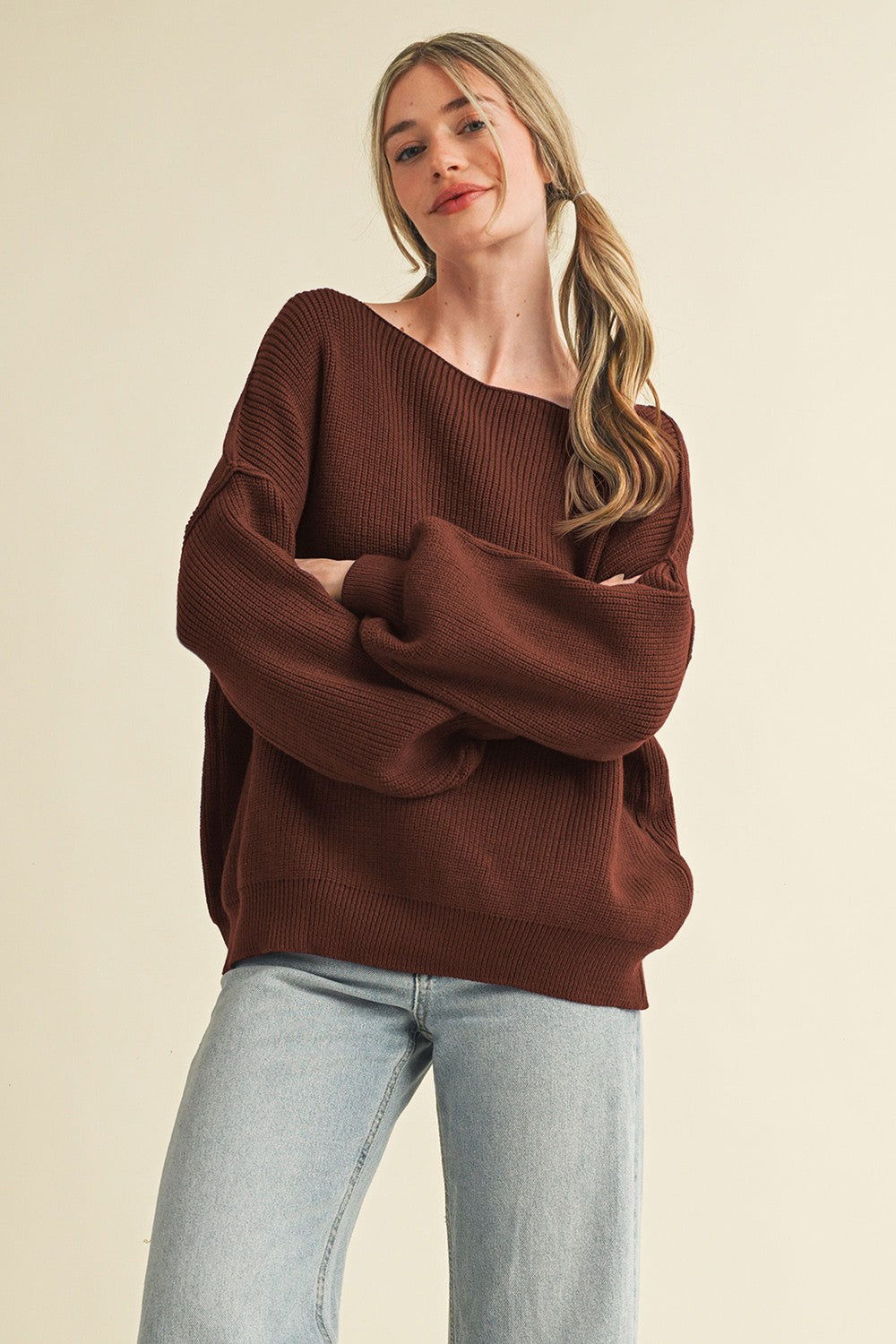 woman wearing a rust-colored oversized ribbed sweater with balloon sleeves and light blue straight leg jeans