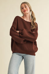 woman wearing a rust-colored oversized ribbed sweater with balloon sleeves and light blue straight leg jeans