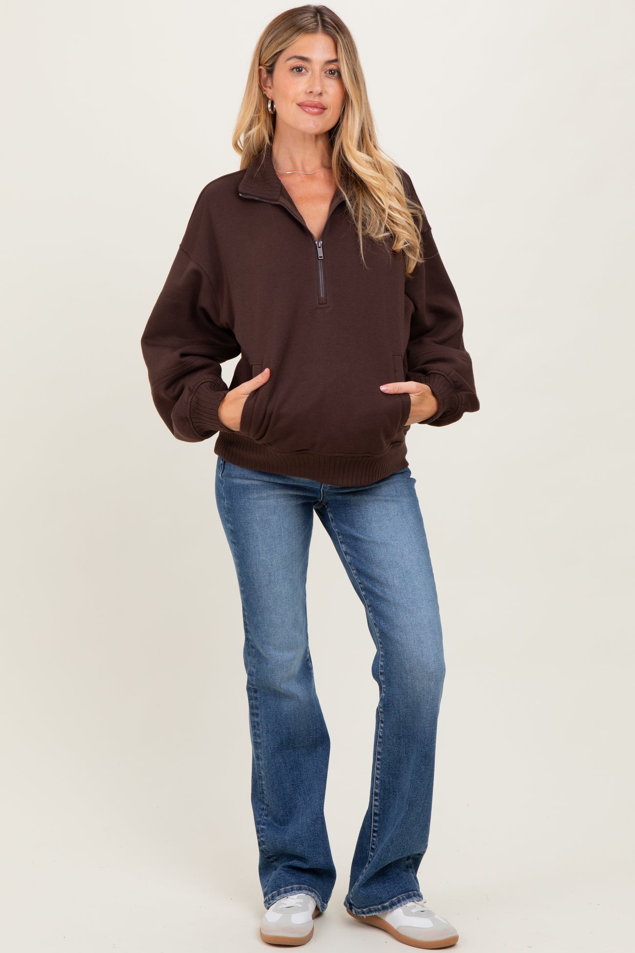 woman wearing a brown zip-up maternity sweatshirt with a relaxed fit and blue flared jeans