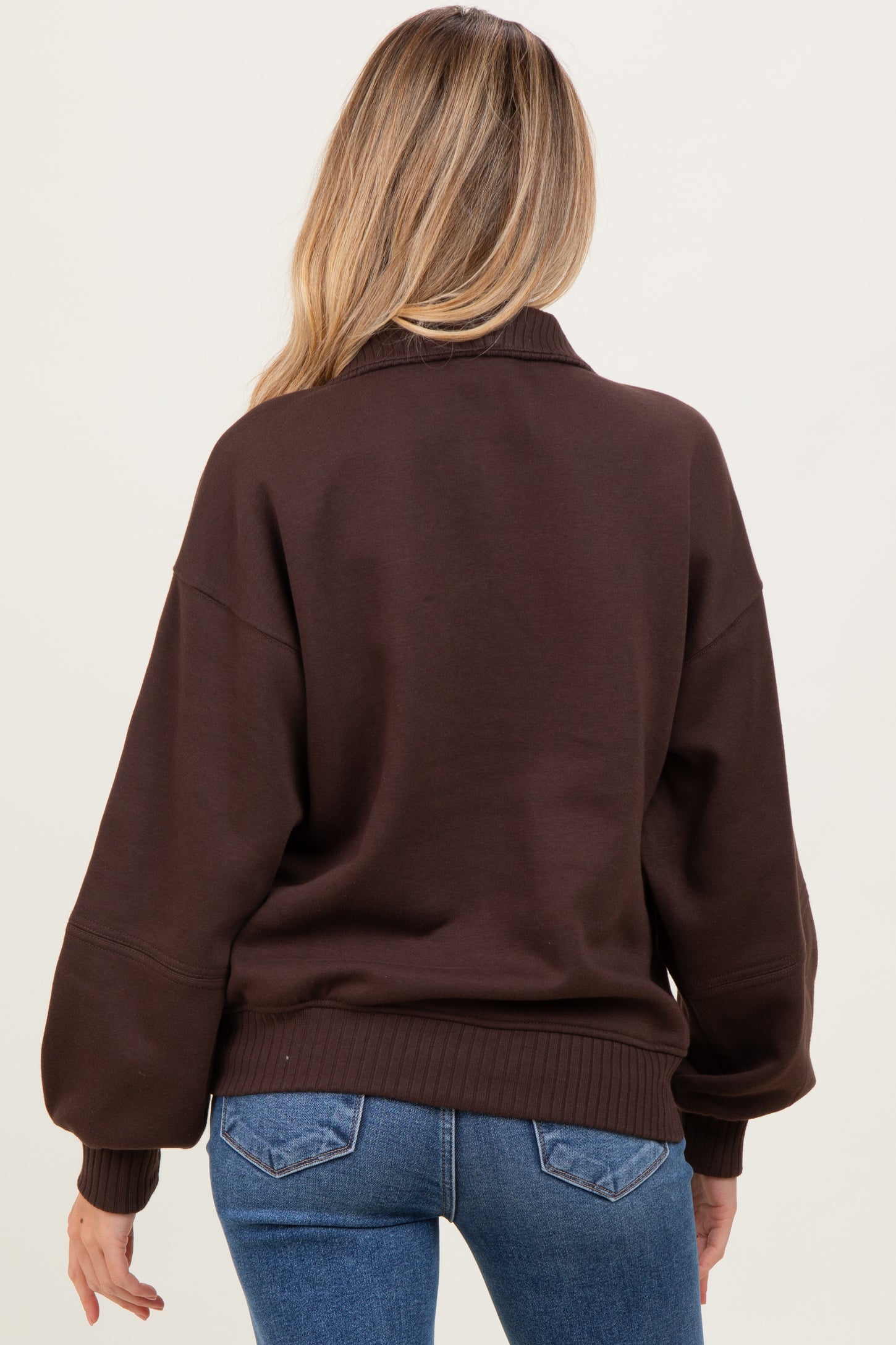 woman wearing a brown oversized maternity sweatshirt, showing the back view with relaxed sleeves and ribbed hem