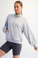 woman wearing a light grey quarter-zip pullover sweatshirt with oversized sleeves and a relaxed fit, paired with black bike shorts